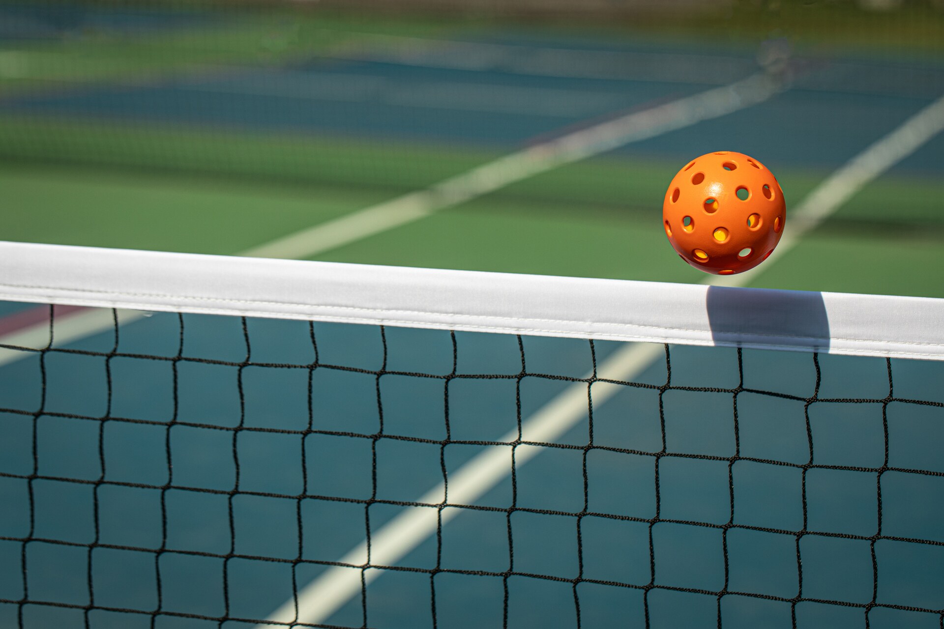 Pickleball sailing over the net on an outdoor court.